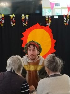 A man performing a play, interacting with two elderly audience members.