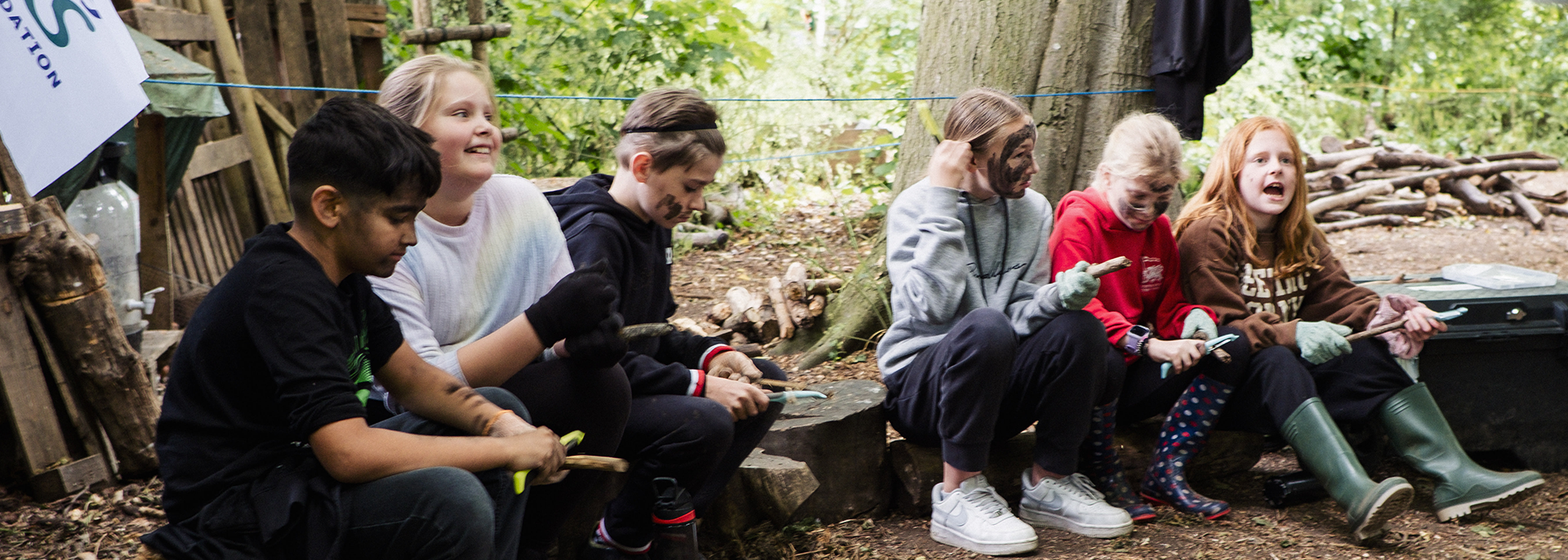 buckingham-sch-group A small group of children sat on a log in a forest school setting.