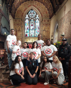 A group of young people with anti-knife crime t shirts are posing for a photo with a police officer in a church building.